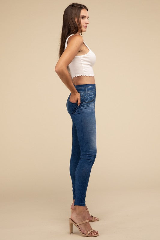 A person wearing Denim Leggings in a high-waisted black design and paired with black heels poses against a plain beige background, highlighting the sleek, stretchy fit.