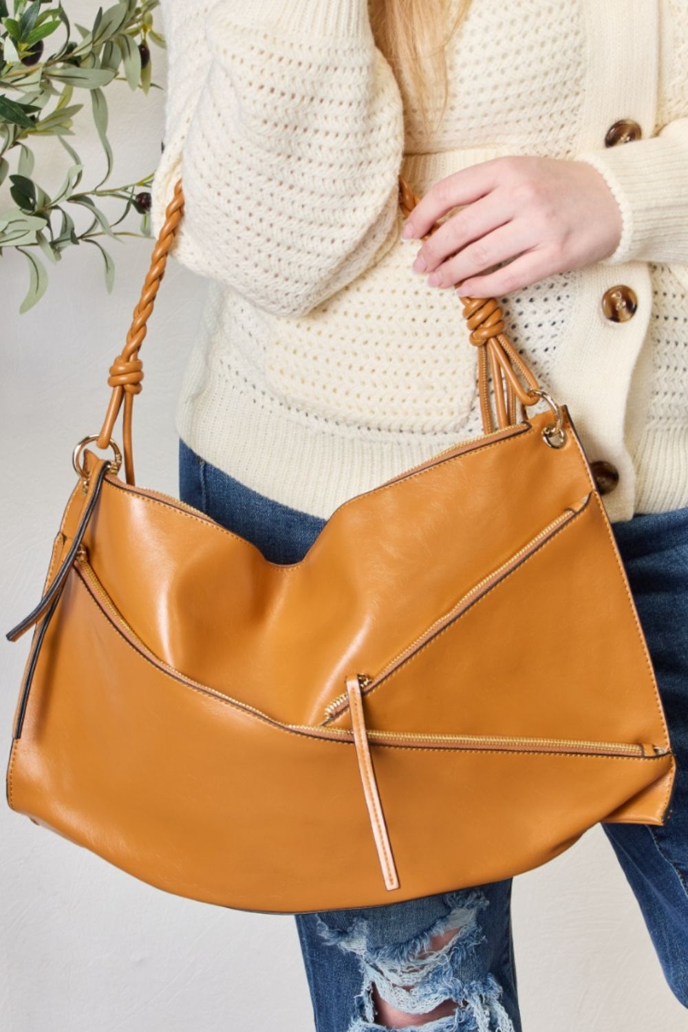 A person in a cream sweater holds a medium-size SHOMICO Zipper Detail Shoulder Bag with gold metal zipper pockets.