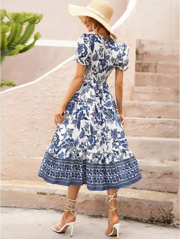 A woman wearing a Women Short Sleeve V Neck Floral Maxi Dress in blue and white, paired with a wide-brimmed hat, stands gracefully on the stairs. She completes her outfit with lace-up sandals.