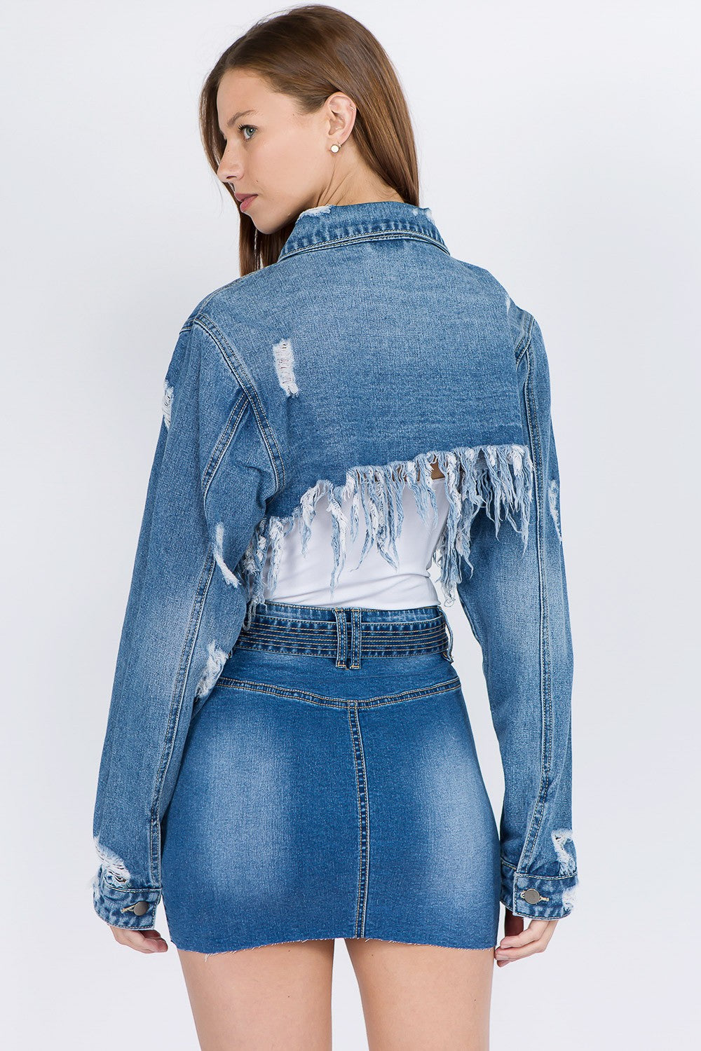 A woman wearing an American Bazi Distressed Denim Jacket with a frayed hem and matching skirt poses against a plain background.