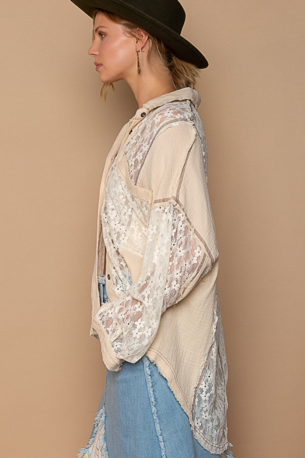 A woman wearing a black wide-brim hat, an oversized POL Lace Button-Down Shirt with intricate lace detailing, and denim pants poses against a beige background.