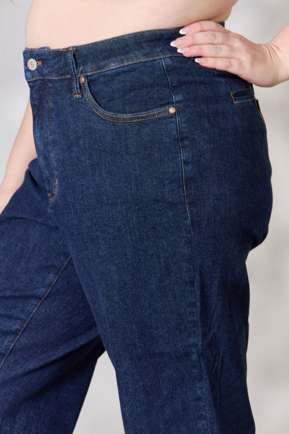 A person wearing the Judy Blue Full Size High Waist Cropped Wide Leg Jeans, which are renowned for their tummy control design, and nude block heel sandals stands near a potted plant.