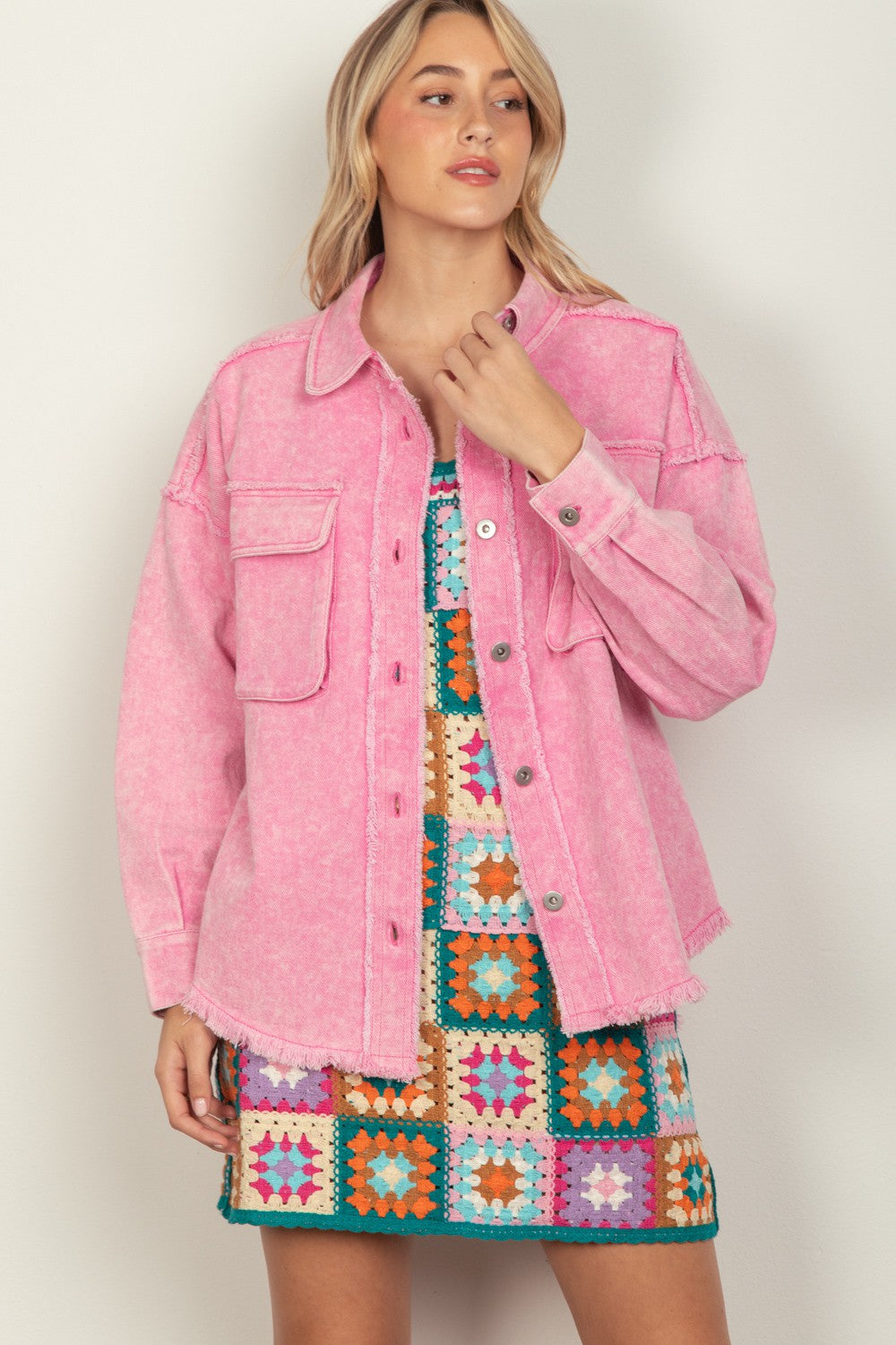 Person wearing a VERY J Full Size Button Up Raw Hem Long Sleeve Jacket in pink over a colorful, patterned dress, standing against a plain background.