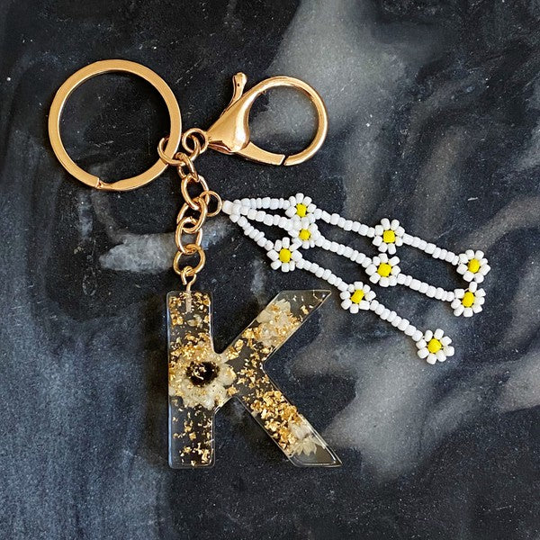 Baby Daisy Initial Key Chain alphabet keychains with real daisy flowers and gold flakes on a marble surface.