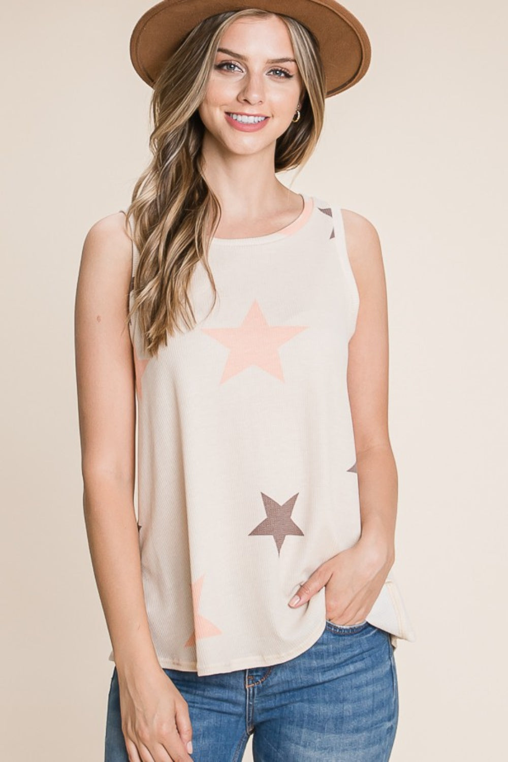 A woman in a BOMBOM Star Print Round Neck Tank and hat smiles at the camera. She is wearing jeans and has one hand in her pocket.