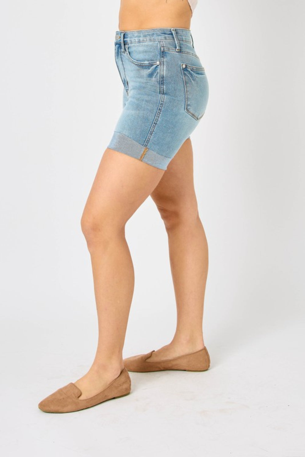 Person wearing Judy Blue Full Size Tummy Control Denim Shorts, which have a flattering fit, paired with brown shoes against a plain white background.