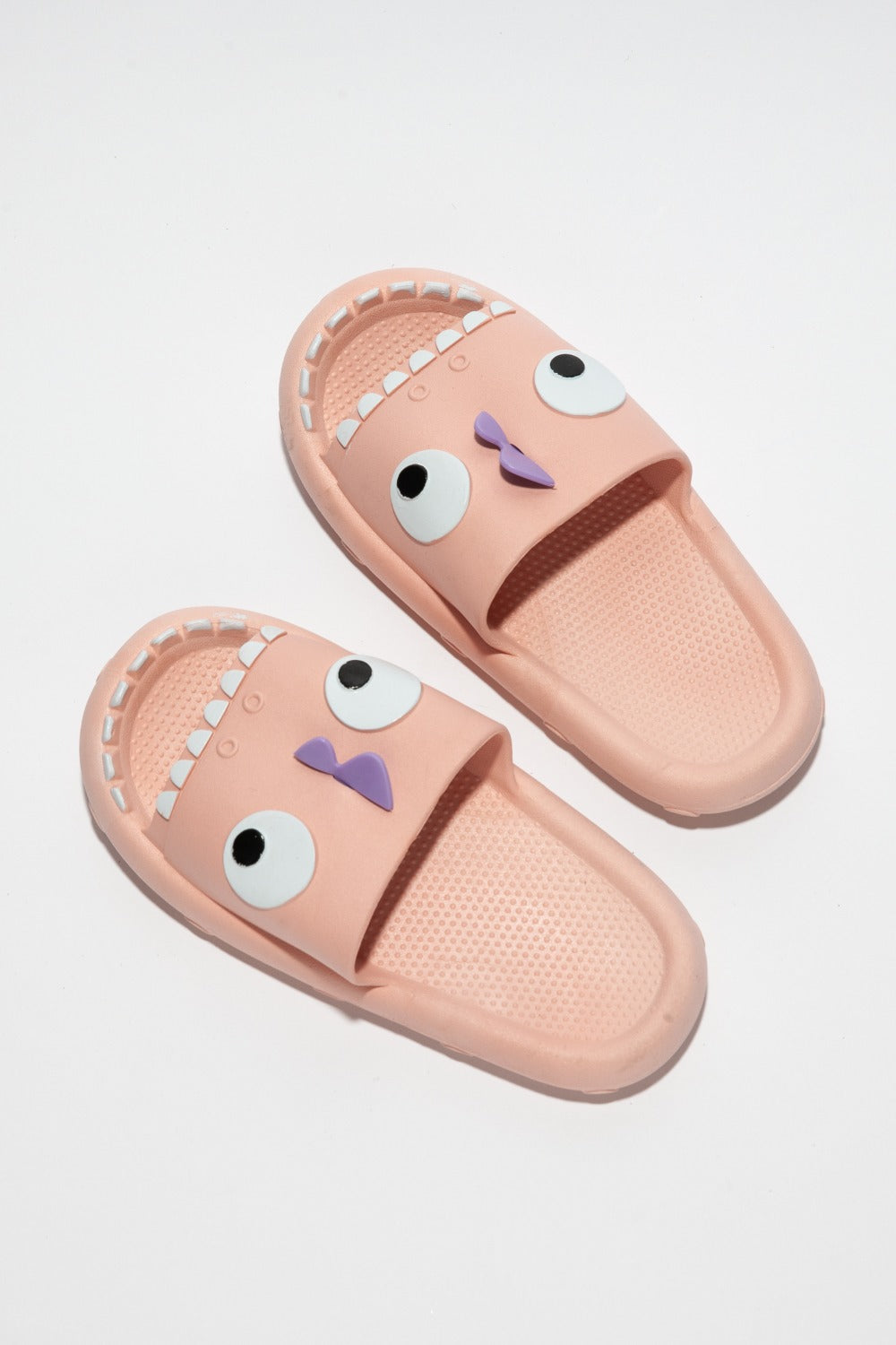 The NOOK JOI Monster Pillow Cloud Slides Non-Slip Slipper features cartoonish monster faces with large eyes, a purple nose, and an open mouth with teeth. Made of durable EVA material, these fun pink cloud slippers also boast an anti-slip design for added safety.