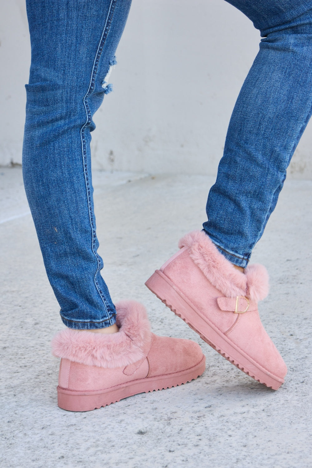 A person stands on a concrete surface, sporting ripped blue jeans and the Forever Link Furry Chunky Thermal Ankle Boots. The furry lining of these fashionable boots suggests both comfort and warmth for winter.