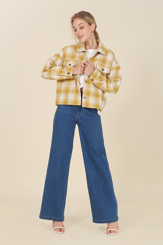 A person wearing a yellow plaid short shacket with pockets and blue jeans, highlighted by a crisp shirt collar, sits against a neutral backdrop.