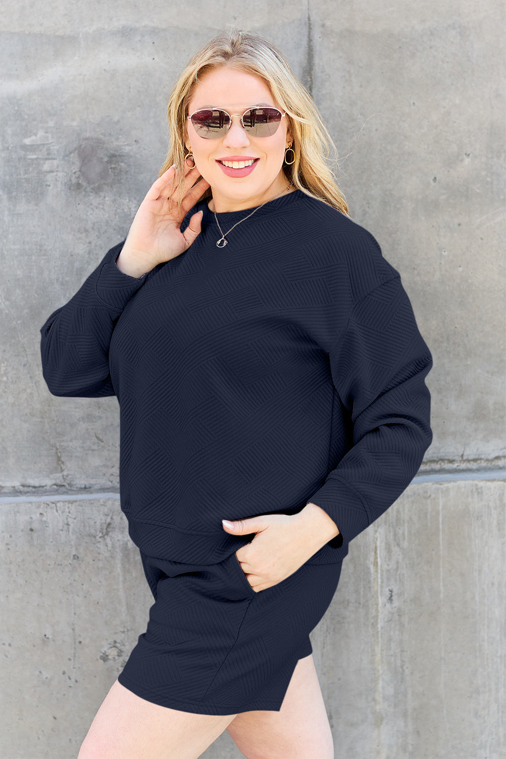 A woman decked out in the Double Take Full Size Texture Long Sleeve Top and Drawstring Shorts Set, featuring a brown textured two-piece with a long-sleeve top and matching pocketed shorts, smiles at the camera.