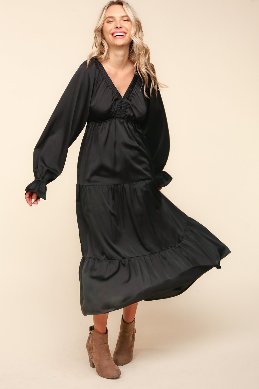 A woman stands wearing the Haptics Flounce Sleeve Tiered Midi Dress with Pockets in black, paired with brown ankle boots, against a plain background.