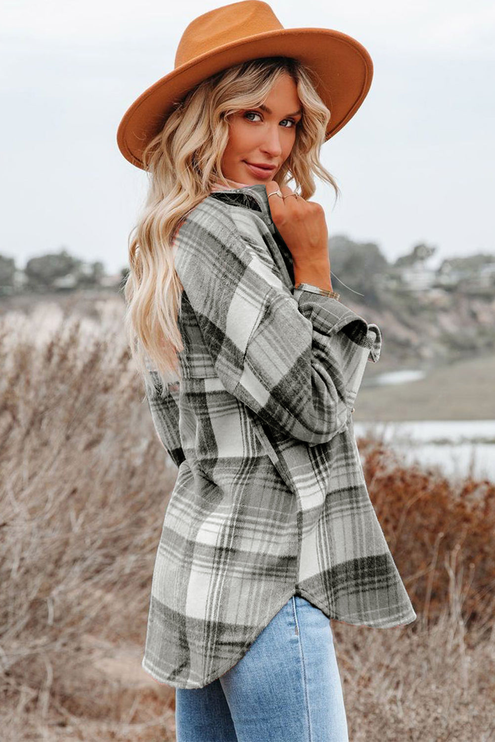A woman wearing a white top, blue jeans, and the Gold Flame & Grey Plaid Button Up Collared Flannel Shacket smiles while posed outdoors.