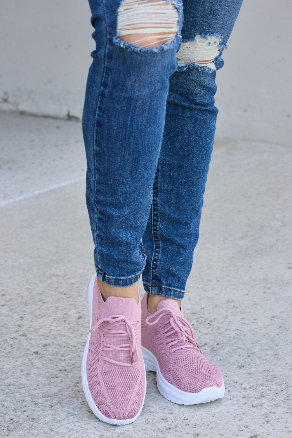 A person is wearing ripped blue jeans and Forever Link breathable mesh lace-up round toe athletic shoes, standing on a concrete surface.