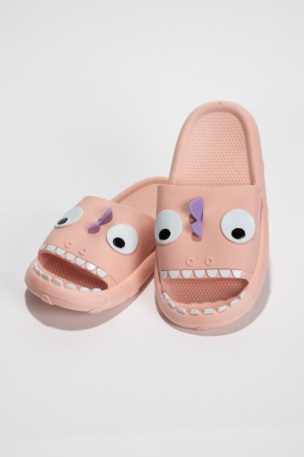 The NOOK JOI Monster Pillow Cloud Slides Non-Slip Slipper features cartoonish monster faces with large eyes, a purple nose, and an open mouth with teeth. Made of durable EVA material, these fun pink cloud slippers also boast an anti-slip design for added safety.