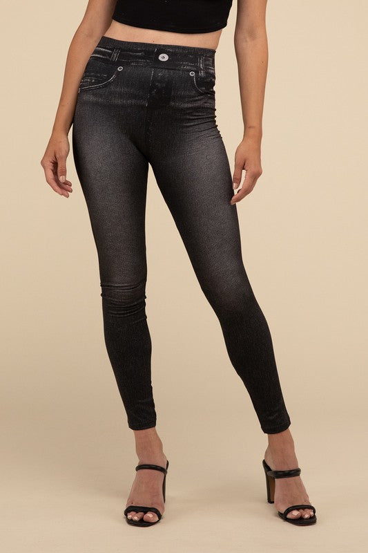 A person wearing Denim Leggings in a high-waisted black design and paired with black heels poses against a plain beige background, highlighting the sleek, stretchy fit.