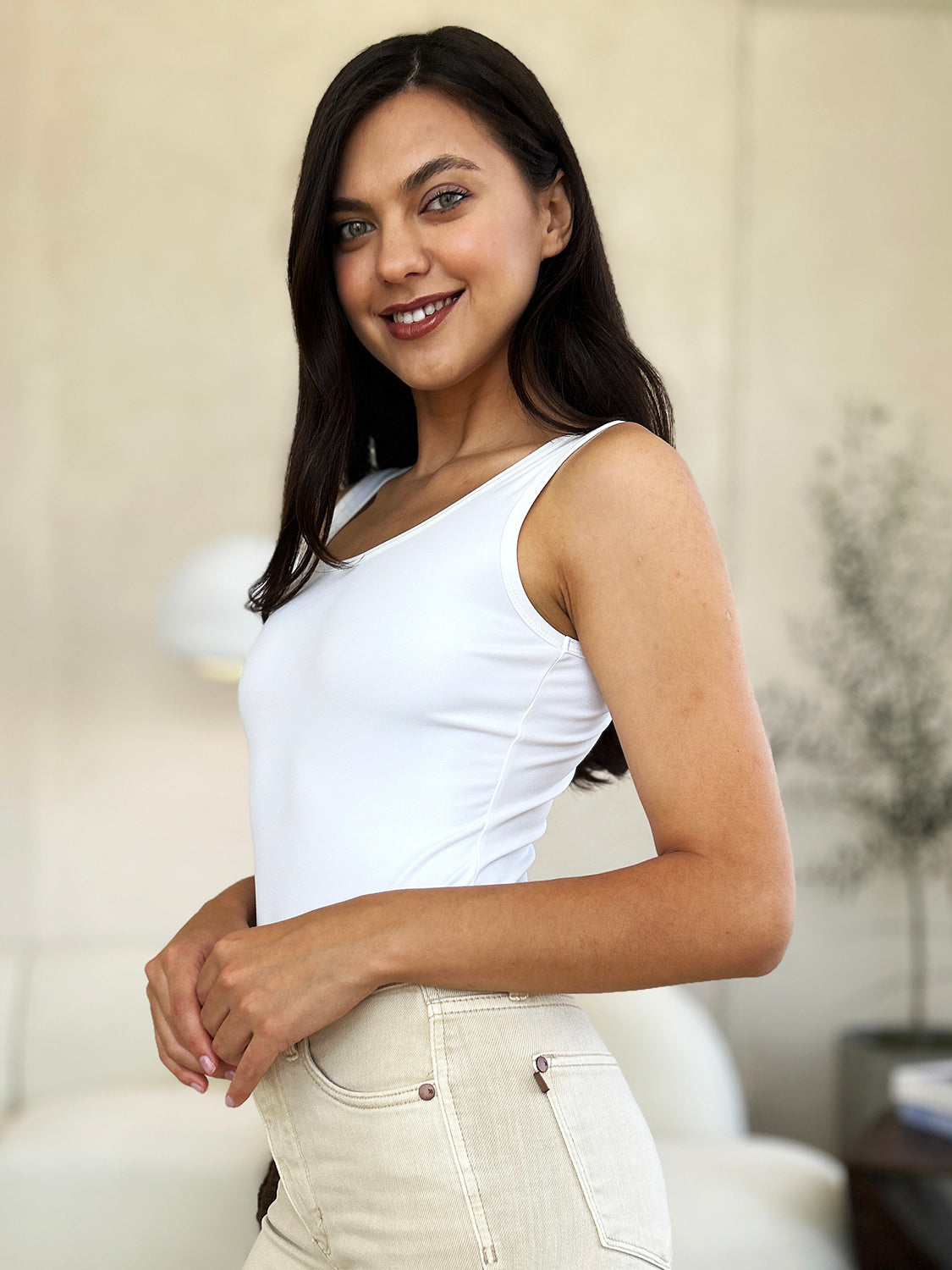 A woman with long, wavy hair stands in front of light-colored curtains, wearing the Basic Bae Full Size Square Neck Sleeveless Bodysuit.