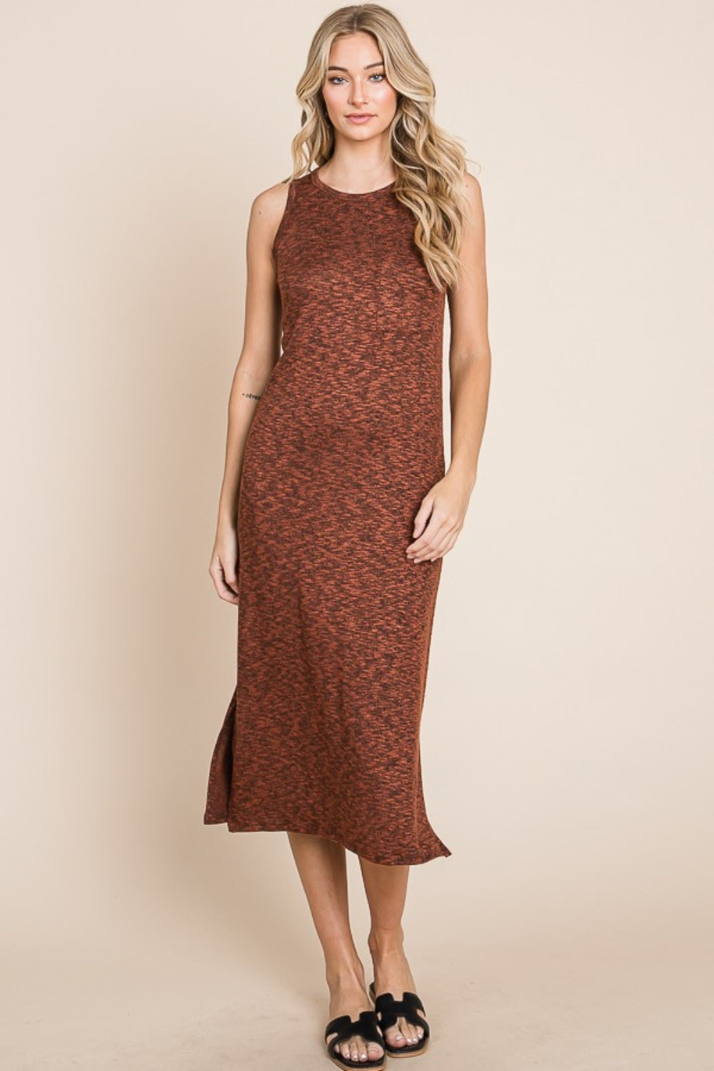 A woman with long blonde hair stands against a beige background, wearing the versatile and stylish BOMBOM Slit Round Neck Sleeveless Midi Dress in rust color, featuring a slit round neck and side slit, paired with black sandals.