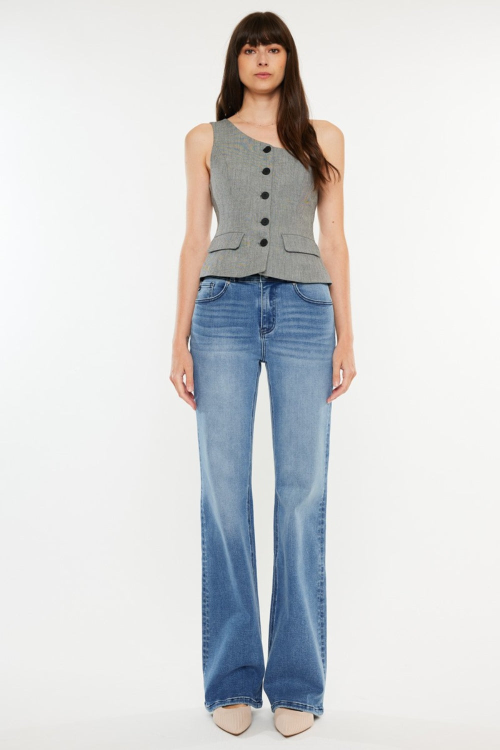 A person stands wearing a sleeveless, buttoned top paired with Kancan Ultra High Rise Cat's Whiskers Jeans. They have long, dark hair and are standing against a plain white background.