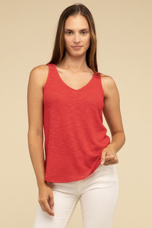 A woman in a stylish and adaptable V Neck Sleeveless Cami Top paired with jeans stands against a beige background. She has long brown hair and maintains a neutral expression.