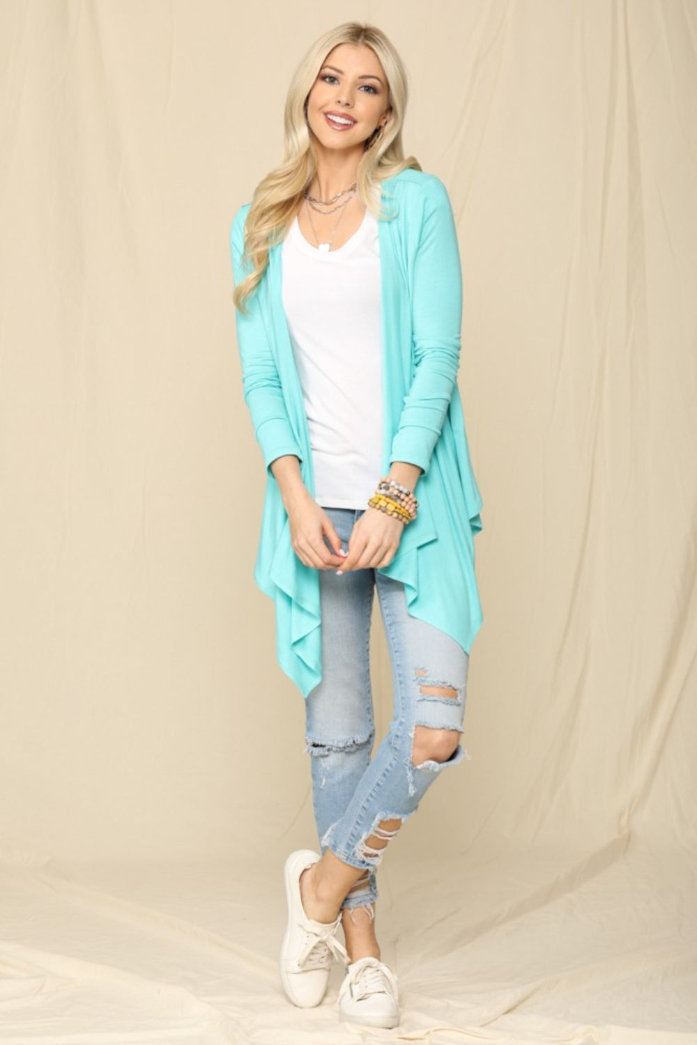 A person is wearing the Celeste Full Size Open Front Knit Cardigan in light blue over a white top and jeans, smiling and standing against a plain background.