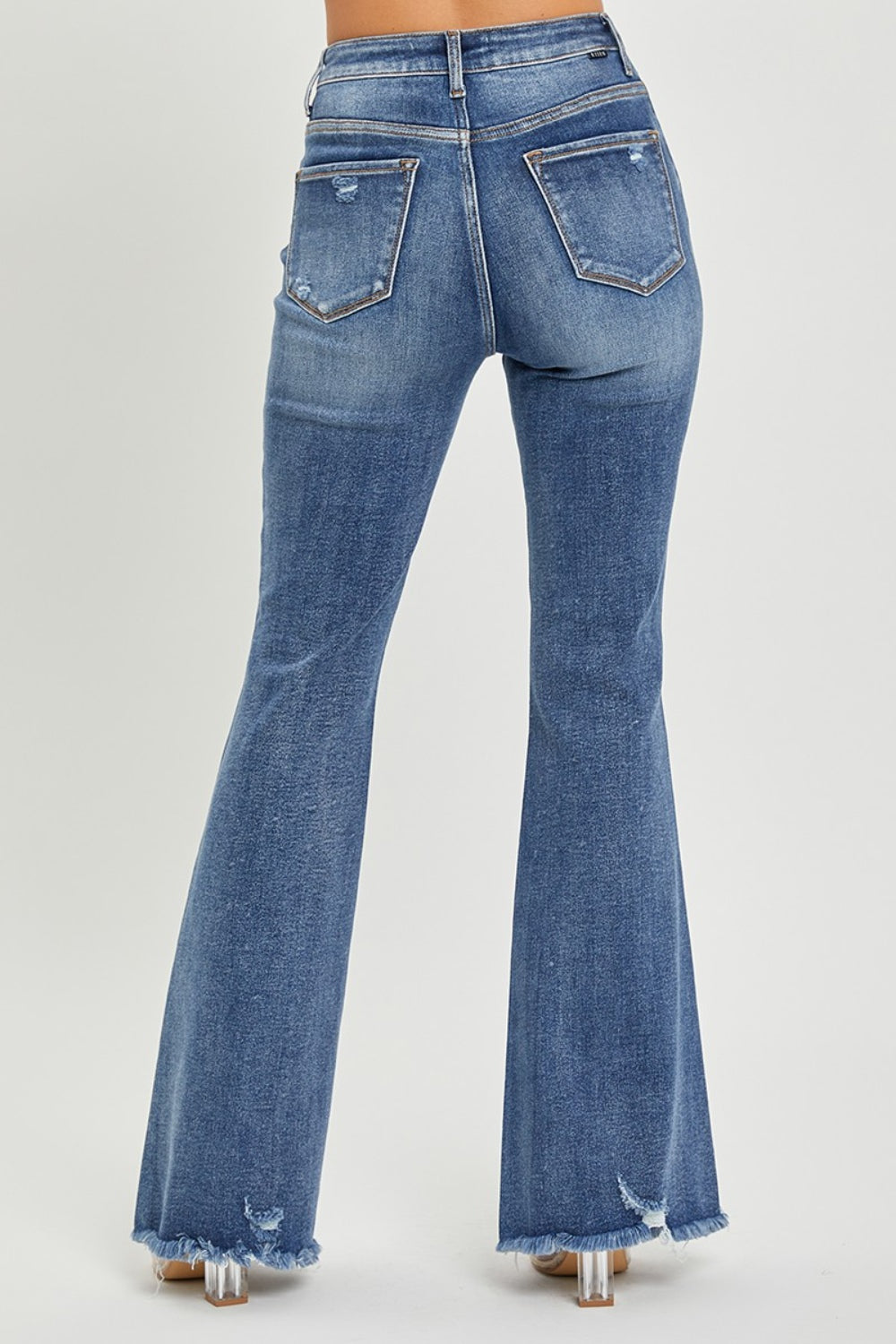 A person is wearing RISEN High Waist Distressed Fare Jeans, characterized by a high-waisted fit with minor rips and frayed hems, standing against a neutral background.