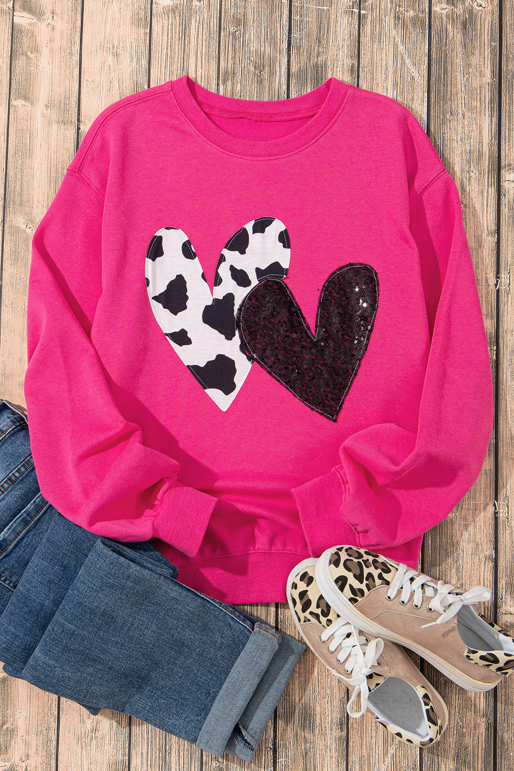 A person with long blonde hair, seen from the back, is wearing a Strawberry Pink Cow & Sequin Double Heart Patch Graphic Sweatshirt and light blue jeans.