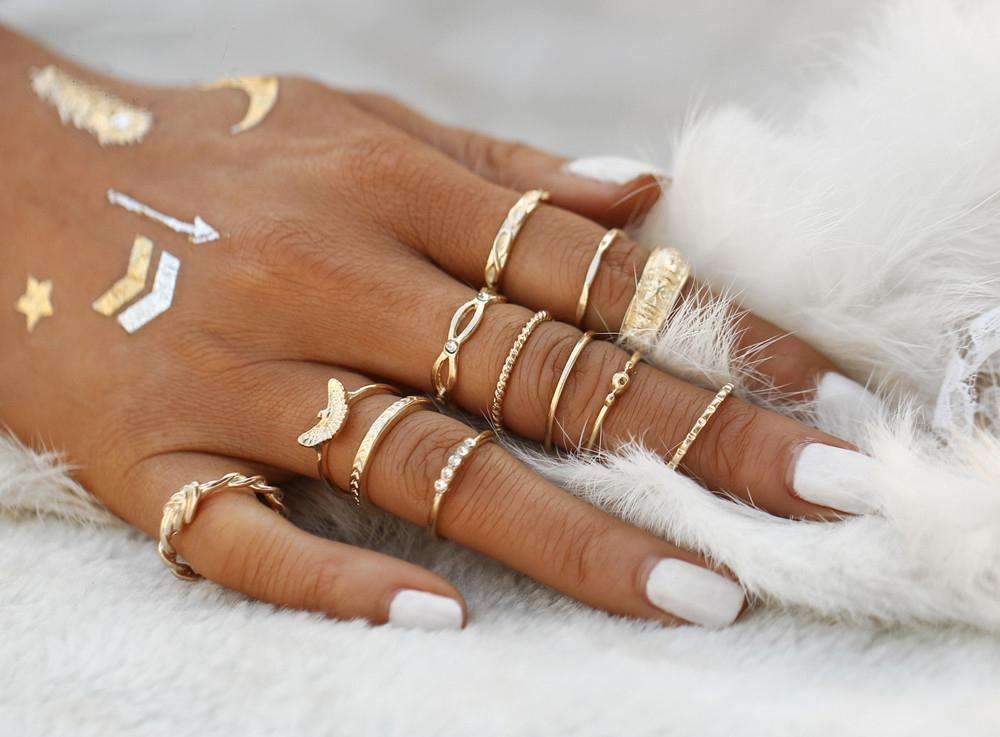 A close-up of a hand adorned with the Golden Ring Set, including a gemstone ring, featuring various designs, against a soft white feathery background.
