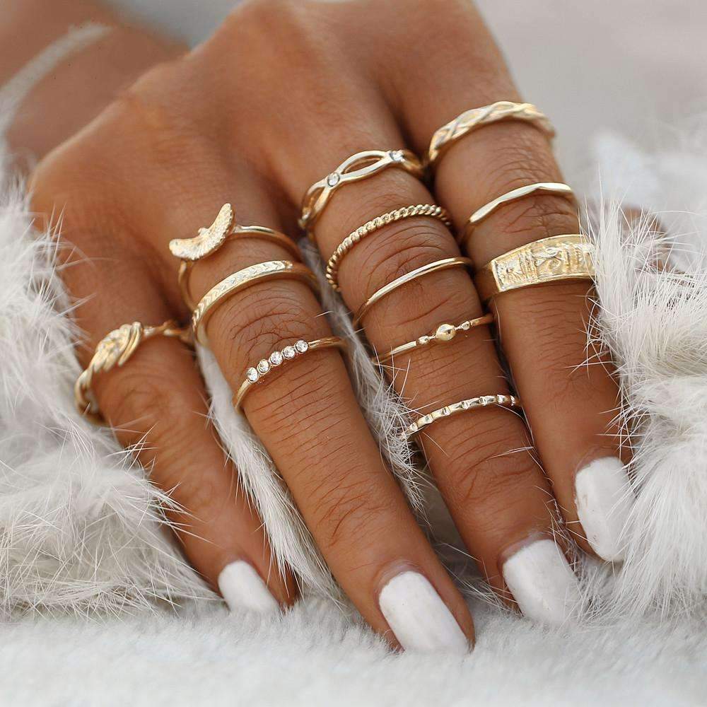 A close-up of a hand adorned with the Golden Ring Set, including a gemstone ring, featuring various designs, against a soft white feathery background.