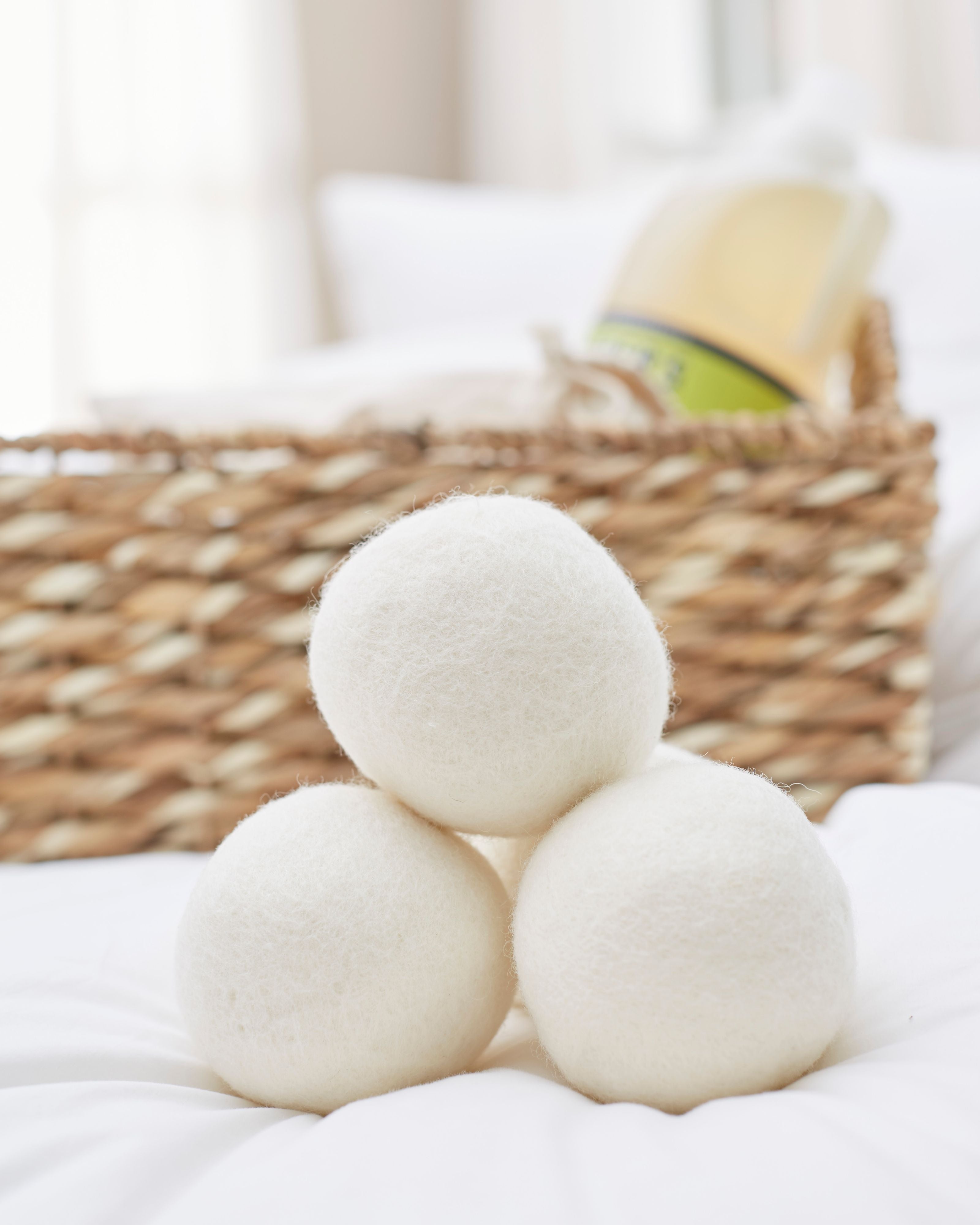 The LanaDown Dryer Balls (Set of 3) are stacked in a pyramid on a bed, accompanied by a woven basket and detergent bottle in the background, to streamline the drying process.