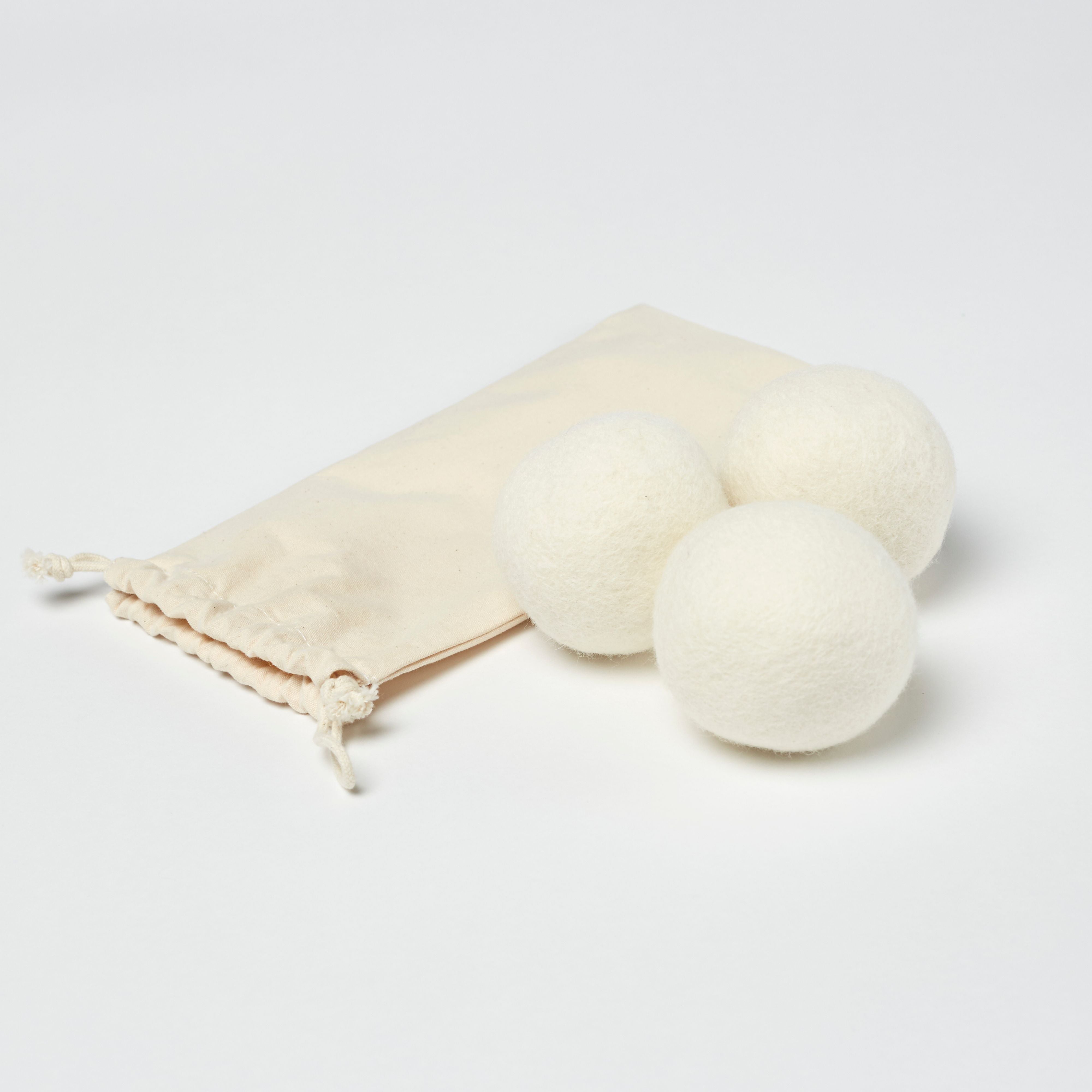 The LanaDown Dryer Balls (Set of 3) are stacked in a pyramid on a bed, accompanied by a woven basket and detergent bottle in the background, to streamline the drying process.