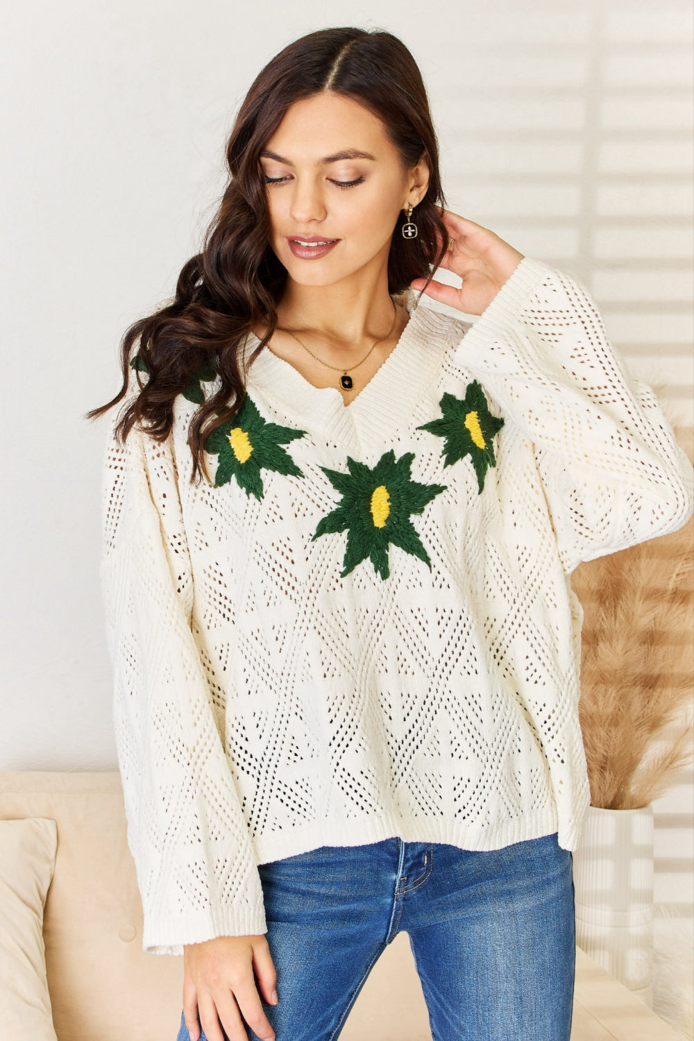 A woman wearing the POL Floral Embroidered Pattern V-Neck Sweater in creamy chenille paired with blue jeans, standing indoors.