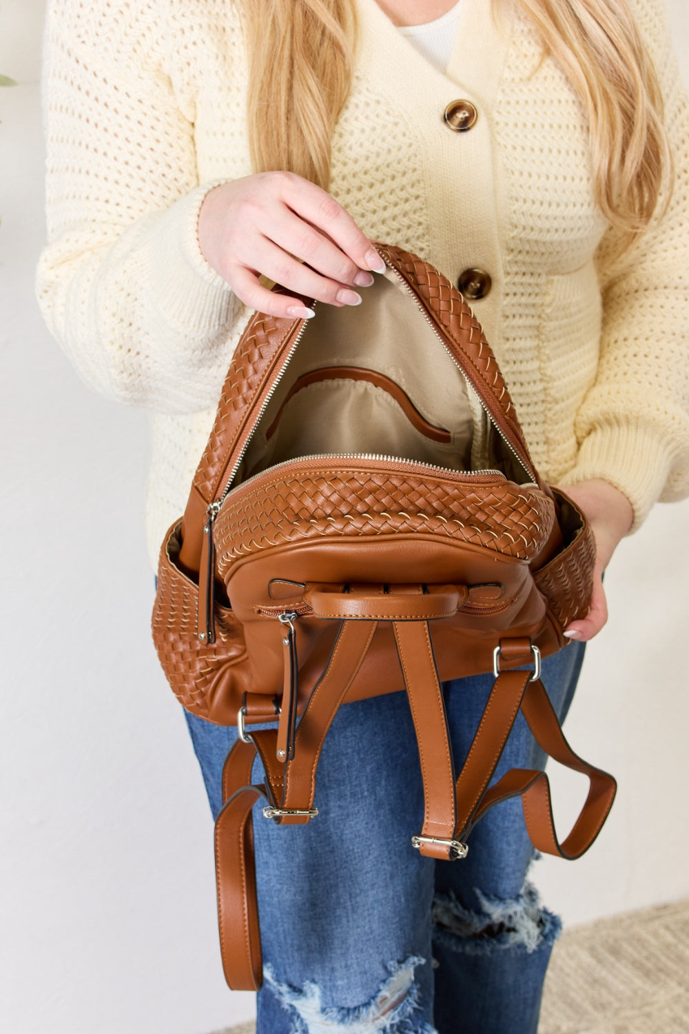 A person wearing a cream sweater and blue jeans carries the SHOMICO PU Leather Woven Backpack, showcasing exquisite craftsmanship with its woven design.