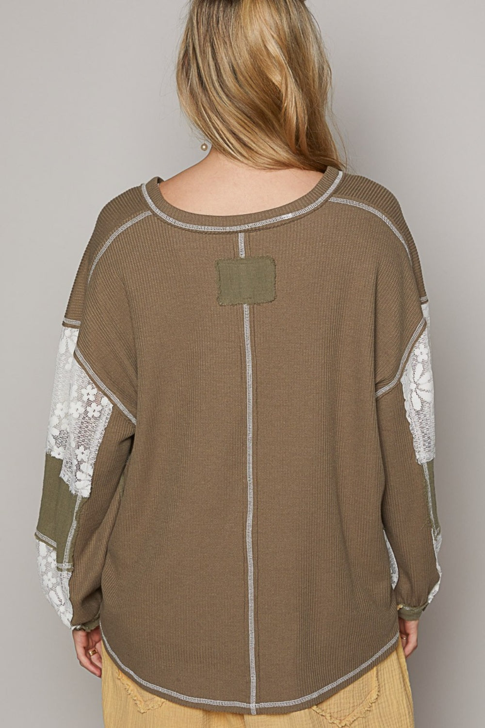 A person stands against a plain background, wearing a loose-fitting, patchwork outfit in shades of brown and beige. The ensemble features the POL V-Neck Lace Balloon Sleeve Exposed Seam Top paired with matching pants. They complete the look with black sandals.