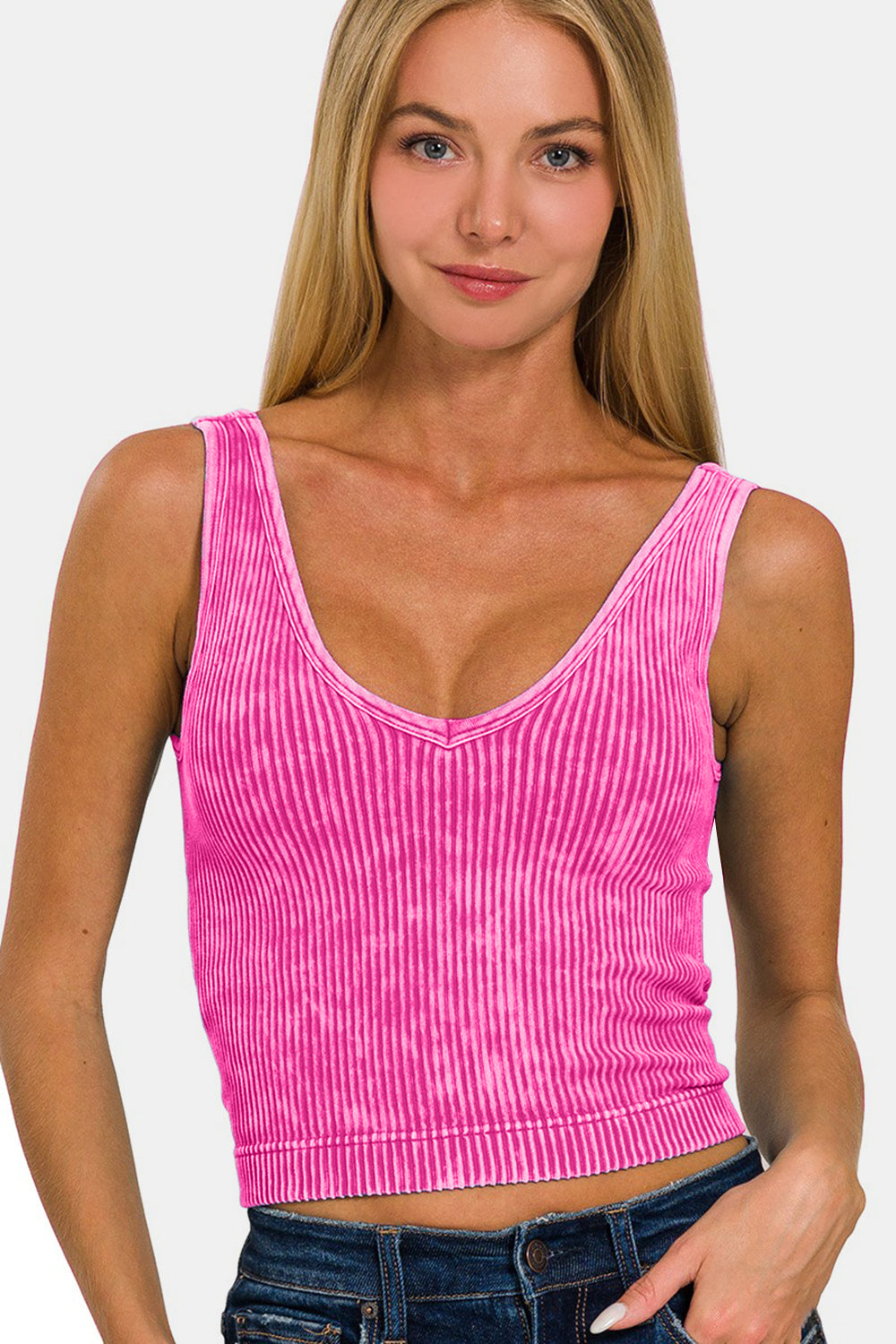 A person wearing the Zenana Washed Ribbed Cropped Bra Padded Tank in a stylish pink stands against a white background, showcasing the comfort of their wardrobe choice.