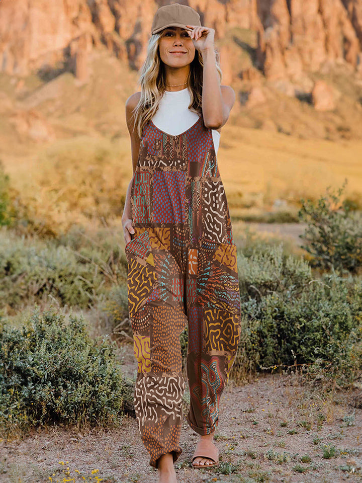 A person standing outdoors in front of rocky terrain, wearing a Full Size Printed V-Neck Sleeveless Jumpsuit and a hat.