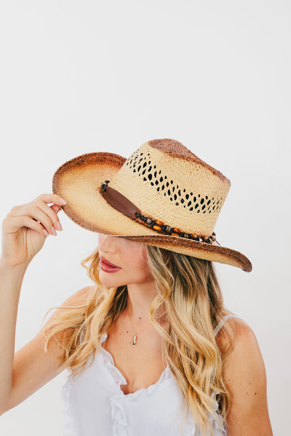 The Fame Cutout Wide Brim Straw Hat is a chic accessory featuring a brown leather band with decorative beads. Its fashionable cutout detailing and patterned, vented crown make it both stylish and functional.