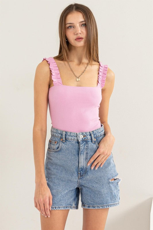 A young woman in a chic Ribbed Ruffle Strap Bodysuit and ripped denim shorts poses against a plain background.