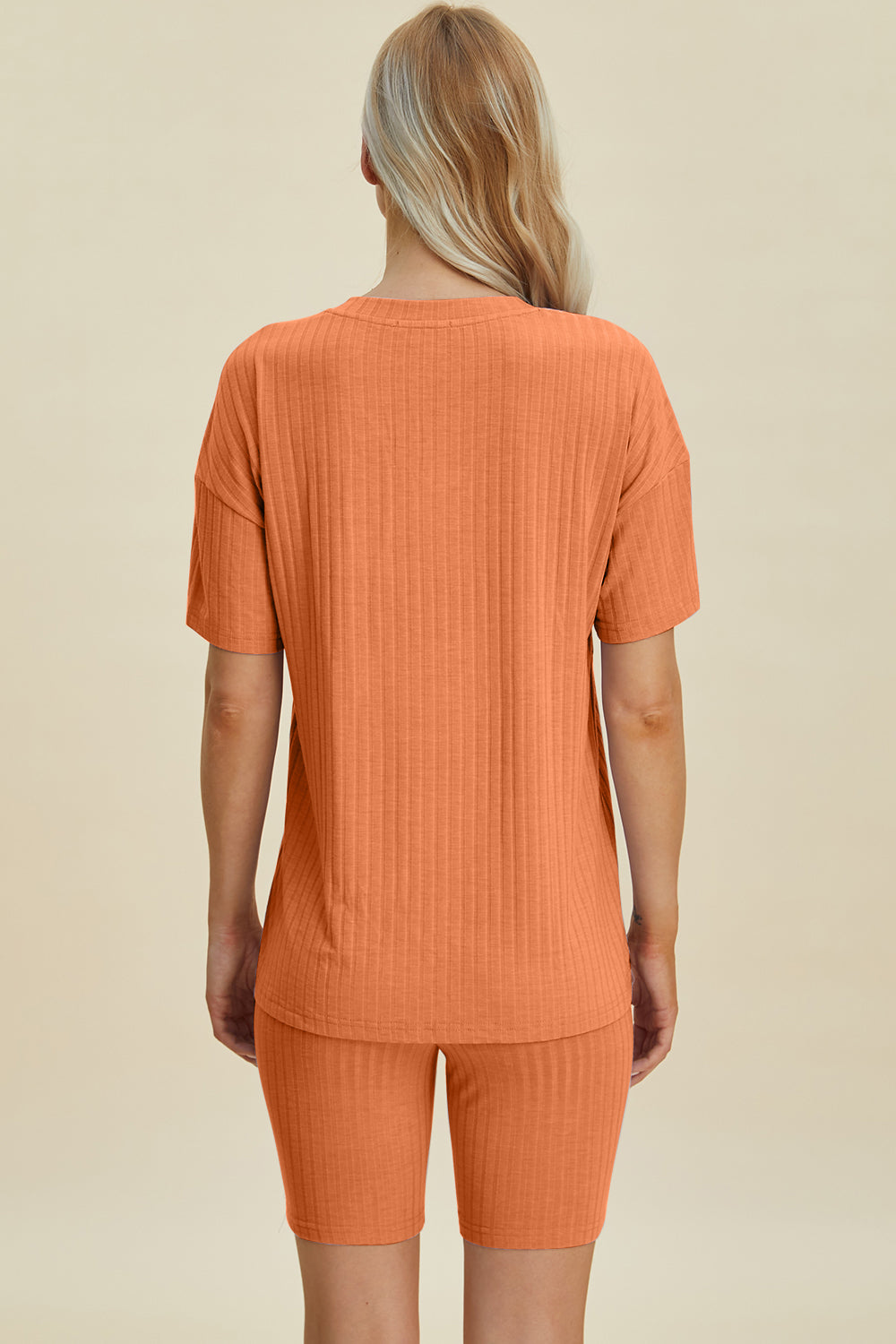 A woman with long blonde hair wearing the Basic Bae Full Size Ribbed V-Neck Short Sleeve Top and Shorts Set in rust stands against a plain background. This stylish two-piece set is made from a comfortable, stretchy fabric that is also machine washable.