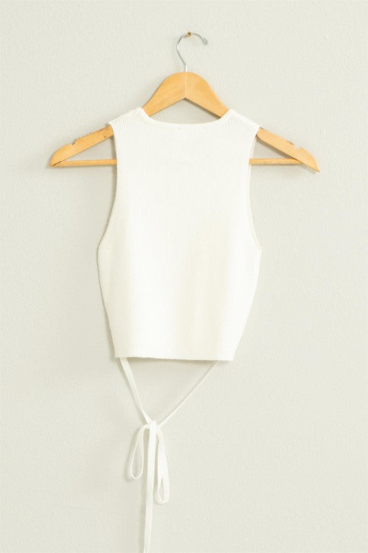 The Good Times Ribbed Sweater Tank Top, featuring a light green color, cropped hem, and back tie, hangs on a wooden hanger against a beige wall.