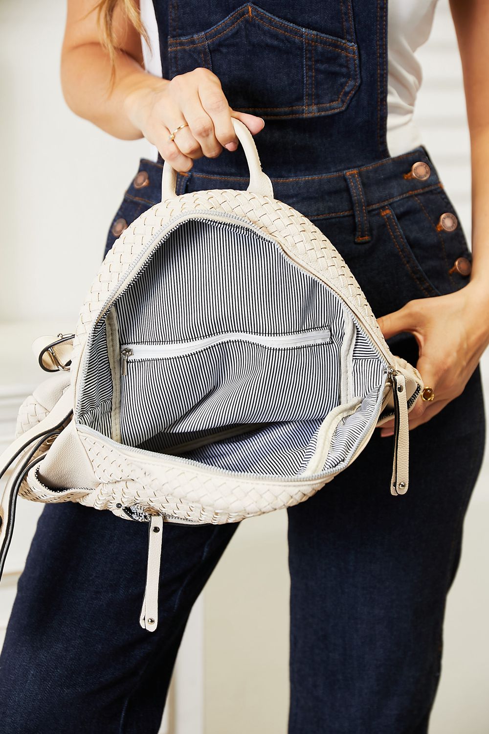 A woman stands indoors smiling, carrying a light-colored SHOMICO PU Leather Backpack on her shoulder while wearing a dark sleeveless top and jeans.