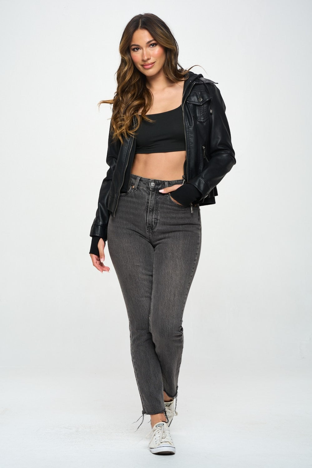 A person with long hair is wearing a sleek Coalition LA Double Zip Hooded Long Sleeve Jacket, paired with a black crop top and gray jeans, standing against a plain background.