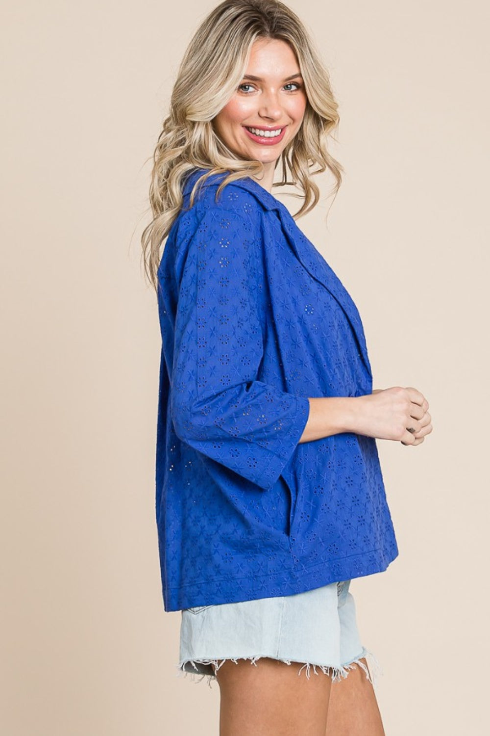 Person smiling, wearing a Culture Code Double Breasted Eyelet Jacket with Pockets over a white top and denim shorts, holding a small textured handbag.