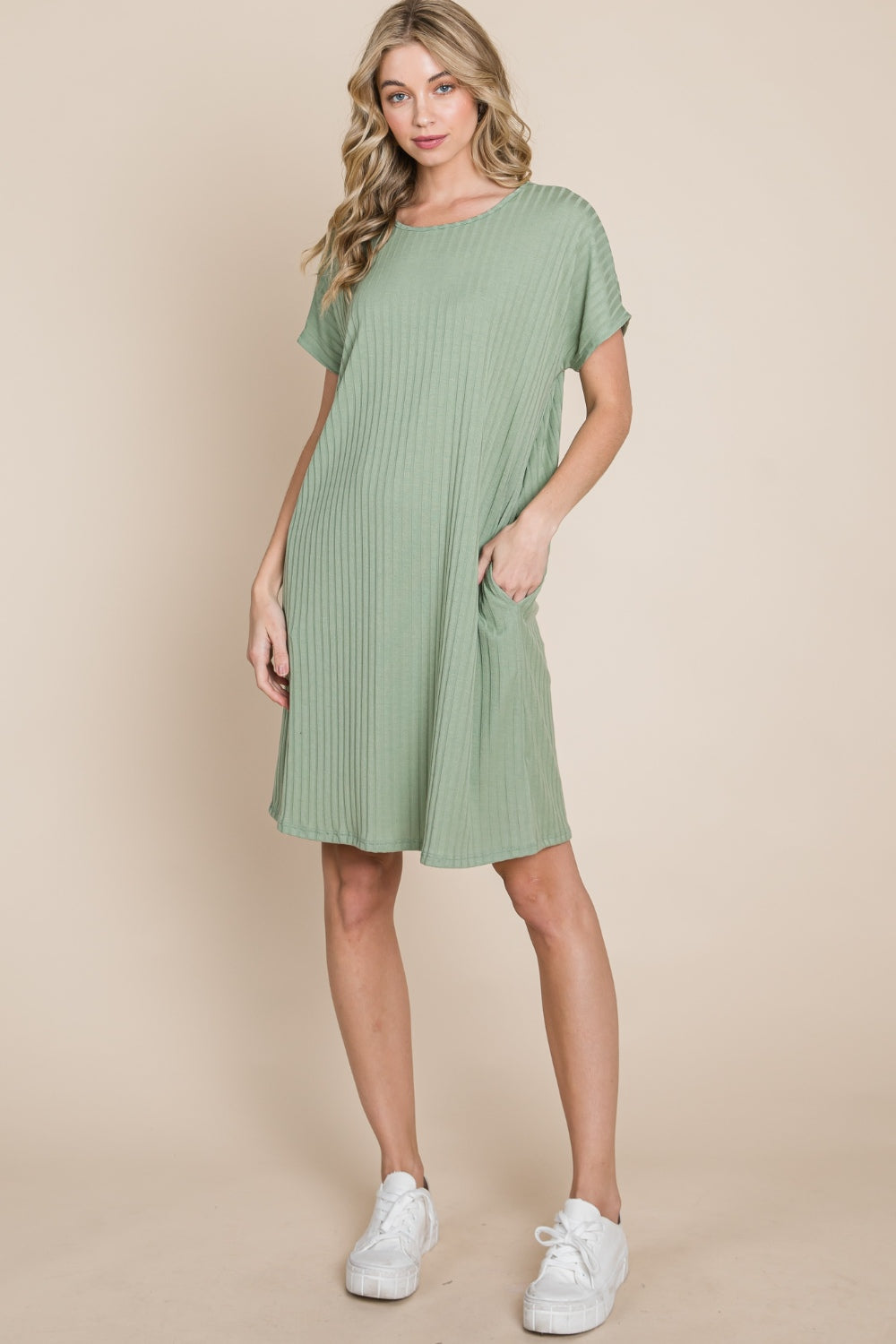 Against a beige background, a person is dressed in the BOMBOM Ribbed Round Neck Short Sleeve Dress in green, featuring a pocket.