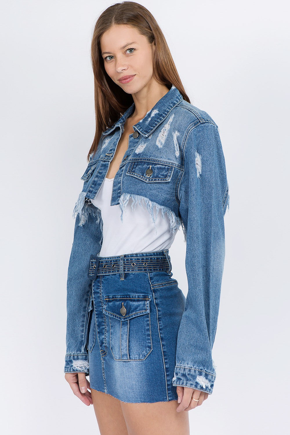 A woman wearing an American Bazi Distressed Denim Jacket with a frayed hem and matching skirt poses against a plain background.