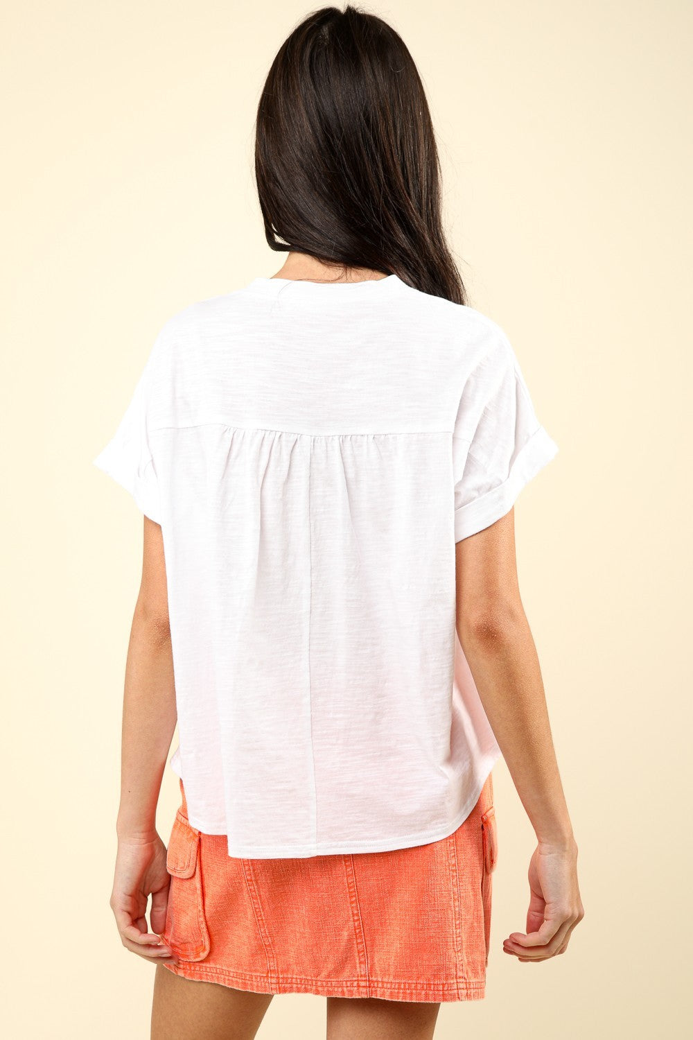 A woman wearing a white, VERY J Notched Short Sleeve Washed T-Shirt paired with an orange skirt poses against a neutral background, showcasing a versatile wardrobe staple.