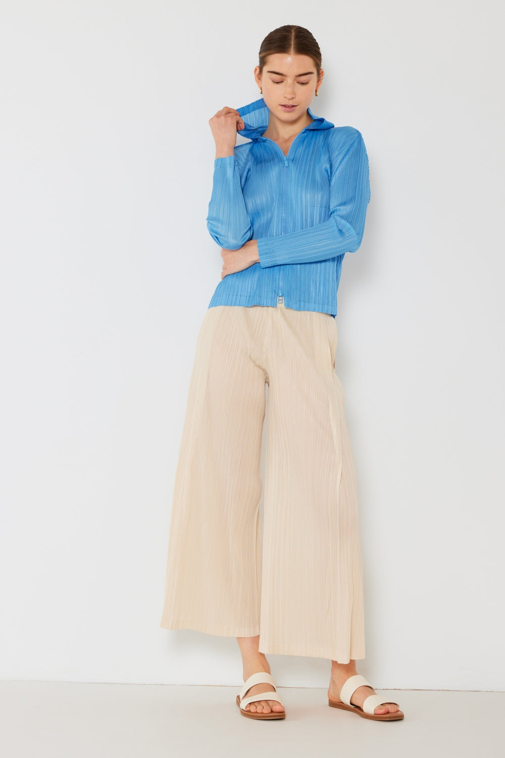 A person wearing the Marina West Swim Pleated Wide-Leg Pants with side pleat detail in red, standing against a white background with hands in pockets and wearing white sandals.