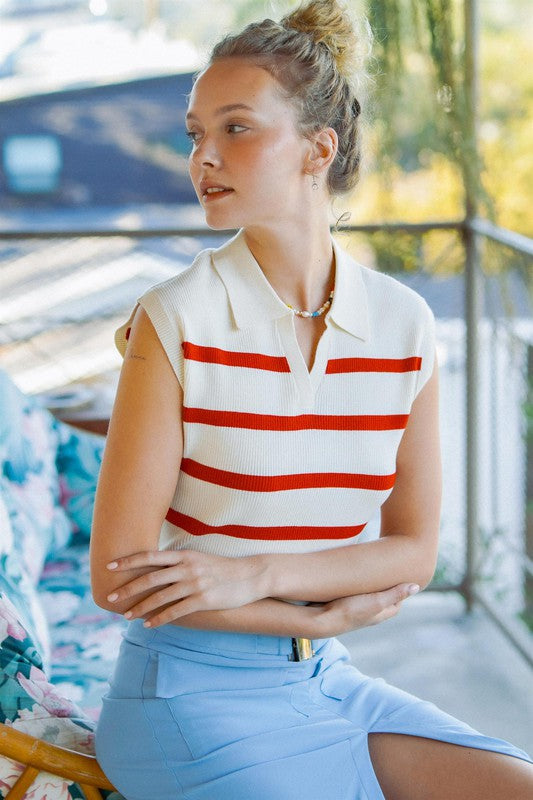 A person sits on a floral couch wearing a Striped Polo Vest with a fitted bodice and a light blue skirt, with their hair tied up.