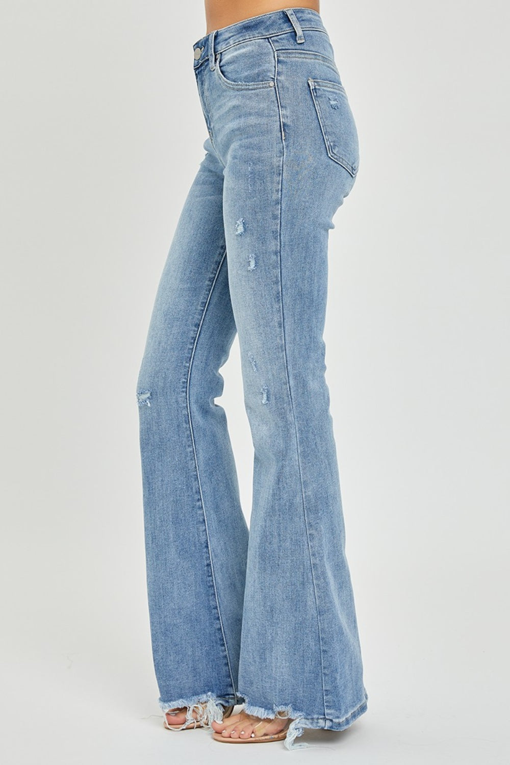 A person wearing the Risen Full Size High Rise Frayed Hem Flare Jeans in light blue with distressed details.