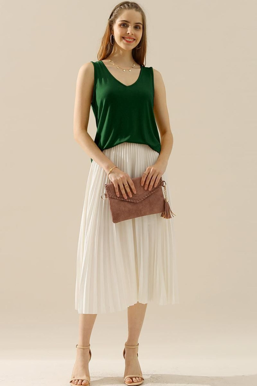 A woman in a stylish and versatile Ninexis Full Size V-Neck Curved Hem Tank and white pleated skirt poses while holding her handbag.