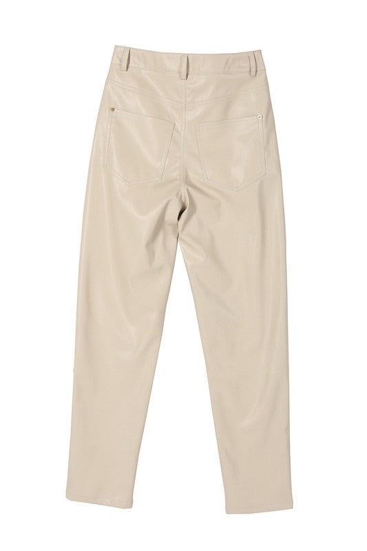 A person wearing a white sweater and black Vegan leather pants with hands in the pockets.